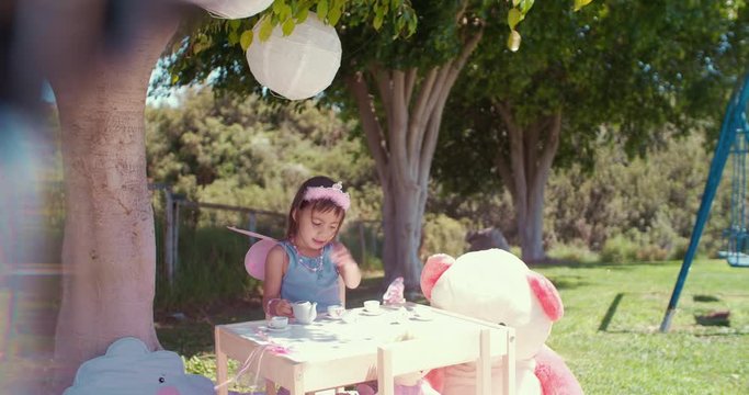 Little Asian girl playing tea party with toys in garden