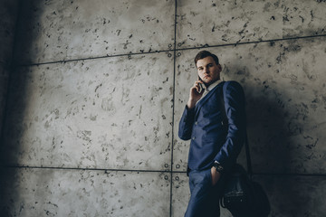 Young businessman using mobile phone while leaning on wall in office