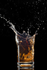 Glass of whiskey with splash isolated on black background