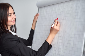 Beautiful smiling young woman writing on a blank flipchart in office as she does a presentation or promotion
