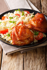 Fried glazed chicken thighs with rice, greens and tomatoes on a close-up. vertical