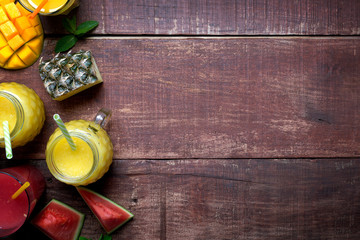 Fresh pineapple and mango smoothie in glasses with fruits on a wooden rustic background with copy space on the right