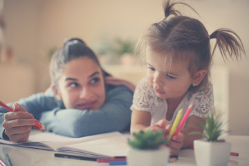 Mother and daughter enjoying together at home and coloring book. Close up.