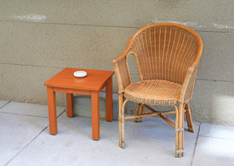 Rattan chairs with mini wooden table against rug cement wall.