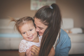 Smiley mother and her little girl in embracing enjoying at home. Close up.