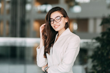 Fototapeta premium Beautiful Russian business girl with glasses, standing with arms crossed and smiling. Office style and business image, business meeting and greeting