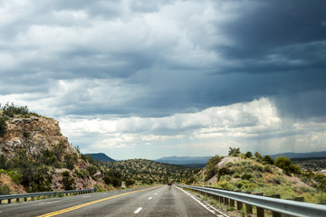 Thunder skyline over rocks and highway. Road going straight ahead, above the road dark thunder sky, around the highway - rocky hills.