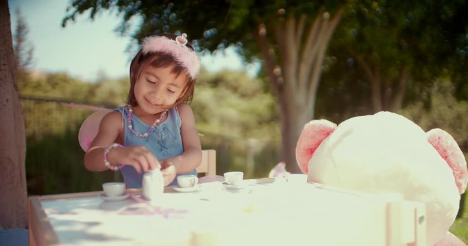 Cute little girl serving tea at pretend garden tea party
