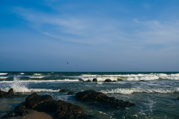 sea with waves and rocks on a cloudy day with kite surfers