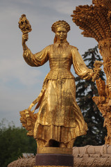 Fototapeta na wymiar Golden statue in Moscow park. A woman with a sheaf in her hand