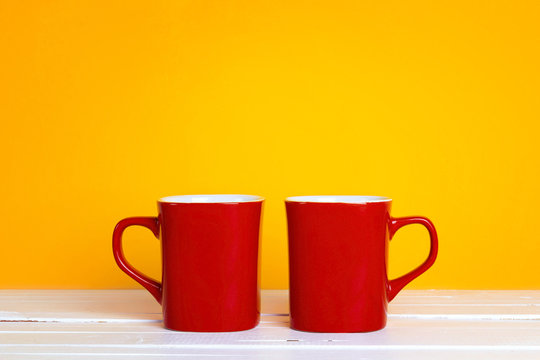 Two red coffee mugs on a yellow background with copt space.