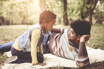 Obraz premium Smiling African American father lying in meadow with daughter and having conversation.