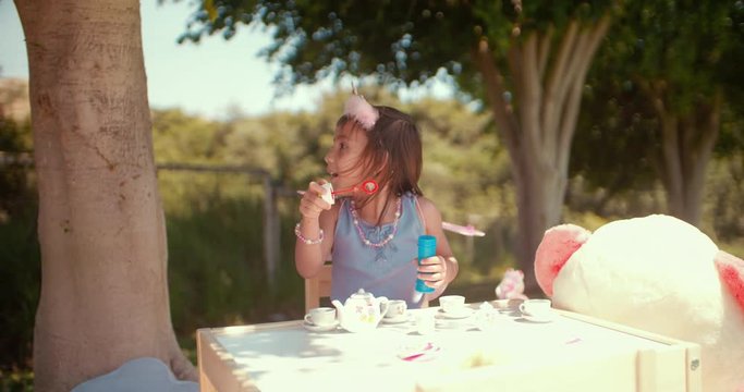 Little Asian girl blowing bubbles at garden tea party