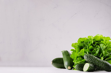 Green vegetables - salad spinach, cucumbers, zucchini on modern white kitchen interior. Healthy vegeterian raw summer food ingredients.