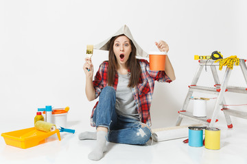 Woman in newspaper hat sitting on floor with brush, paint can, instruments for renovation apartment isolated on white background. Wallpaper, accessories for gluing, painting tools. Repair home concept