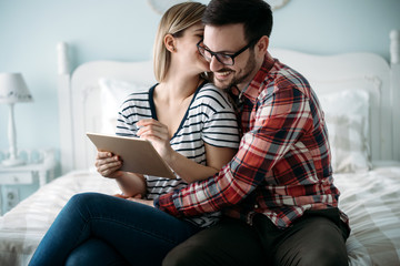 Young happy couple using tablet in bedroom