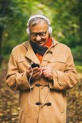 Senior man listening music in park in autumn. 