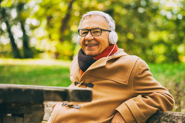 Fototapeta premium Senior man listening music in park in autumn. 
