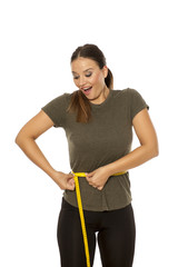 Happy young woman measuring her waist on white background