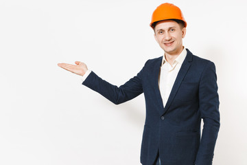 Young handsome successful businessman in dark suit, protective hardhat pointing hand aside on copy space isolated on white background. Male worker for advertisement. Business, working concept.