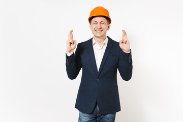 Young businessman in dark suit, protective hardhat keeping fingers crossed and eyes closed and waiting for special moment isolated on white background. Making a wish. Male worker for advertisement.