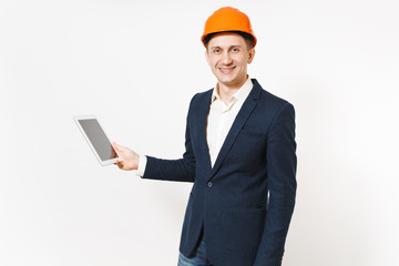 Young handsome smiling businessman in dark suit, protective hardhat holding tablet pc computer with blank screen isolated on white background. Male worker for advertisement. Business, working concept.