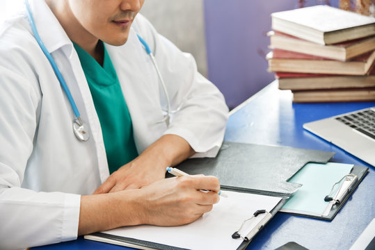 Asian male doctor is writing something on clipboard.