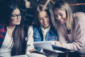 Three students girl reading file together indoors. Close up.