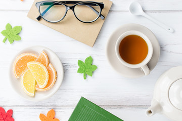 Feminine desk workspace flat lay with diary, eyeglasses, book, tea mug, sweets and felt decor.