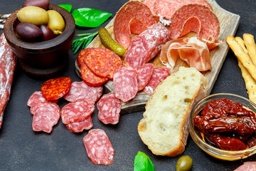 Cutting board with salami, bread, olives and capers