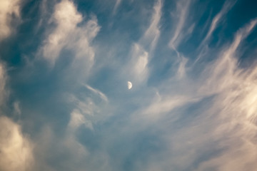 Dramatic blue skies and clouds with the moon in the center, a surreal landscape