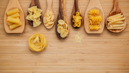 Italian foods concept and menu design. Various kind of Pasta Farfalle, Pasta A Riso, Orecchiette Pugliesi, Gnocco Sardo and Farfalle in wooden spoons setup on bamboo cutting board with flat lay.