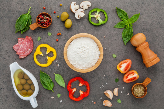 The ingredients for homemade pizza with ingredients sweet basil ,tomato ,garlic ,bay leaves ,pepper ,onion and mozzarella cheese on dark stone background with flat lay.