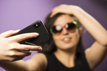 Young Woman Make Selfie in Sunglasses on Purple Background. Photo in Googles on the Latest Smartphone