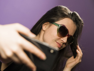 Young Woman Make Selfie in Sunglasses on Purple Background. Photo in Googles on the Latest Smartphone