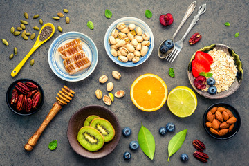 Ingredients for the healthy foods background Mixed nuts, honey, berries, fruits, blueberry, orange, almonds, oatmeal and chia seeds .The concept of healthy food set up on dark stone background.