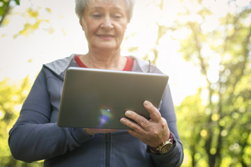 Cheerful senior woman in sports clothing after exercise using digital tablet. Focus is on hand.