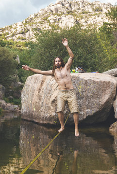 Mid aged man with drealocks practice slack line over the water in a lake in La Pedriza, Spain