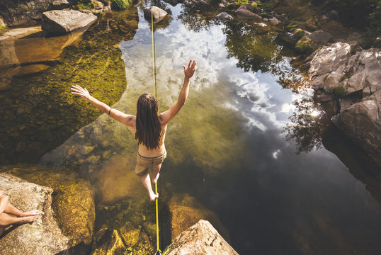 Slackliner with drealocks practicing slack line over water