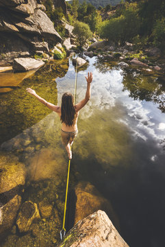 Back view of slackliner with drealocks practicing slack line over the water in a lake in La Pedriza, Spain
