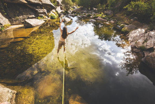 Back view of slackliner with drealocks practicing slack line over the water in a lake in La Pedriza, Spain