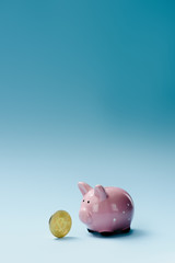 close up view of pink piggy bank and golden bit coin on blue backdrop