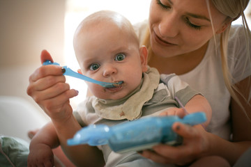 Mother feeding her little baby boy at home. Close up.