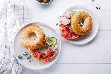 Bagel with salmon fish, cream cheese, cucumber and fresh radish slices on white wooden background