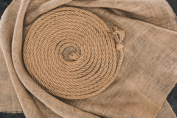 Fototapeta na wymiar top view of brown nautical rope arranged in circle on sackcloth on dark concrete surface
