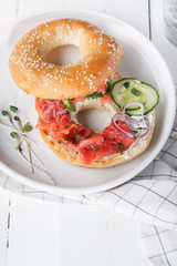 Bagels with salmon fish, cream cheese, cucumber and fresh radish slices on white wooden background