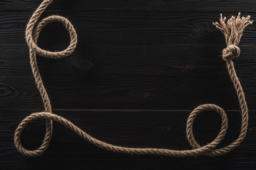 top view of brown nautical rope with knot on dark wooden surface