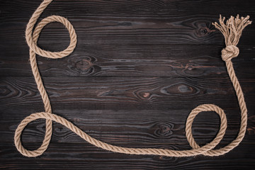 top view of brown nautical rope with knot on dark wooden surface