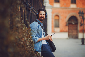 Handsome young man listen to music via smartphone and headphones on the street