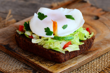Homemade egg poached sandwich. Egg poached on rye bread slice with fresh vegetables and parsley. Healthy breakfast. Wooden background. Rustic style. Closeup